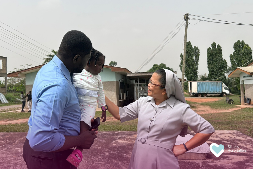 Sister Hospitaller speaking with a family while holding a child in a community setting