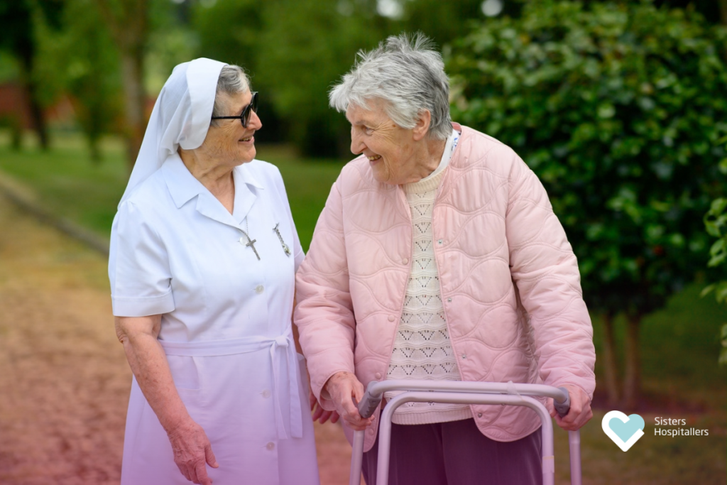 Sister Hospitaller walking with an elderly woman in a moment of companionship